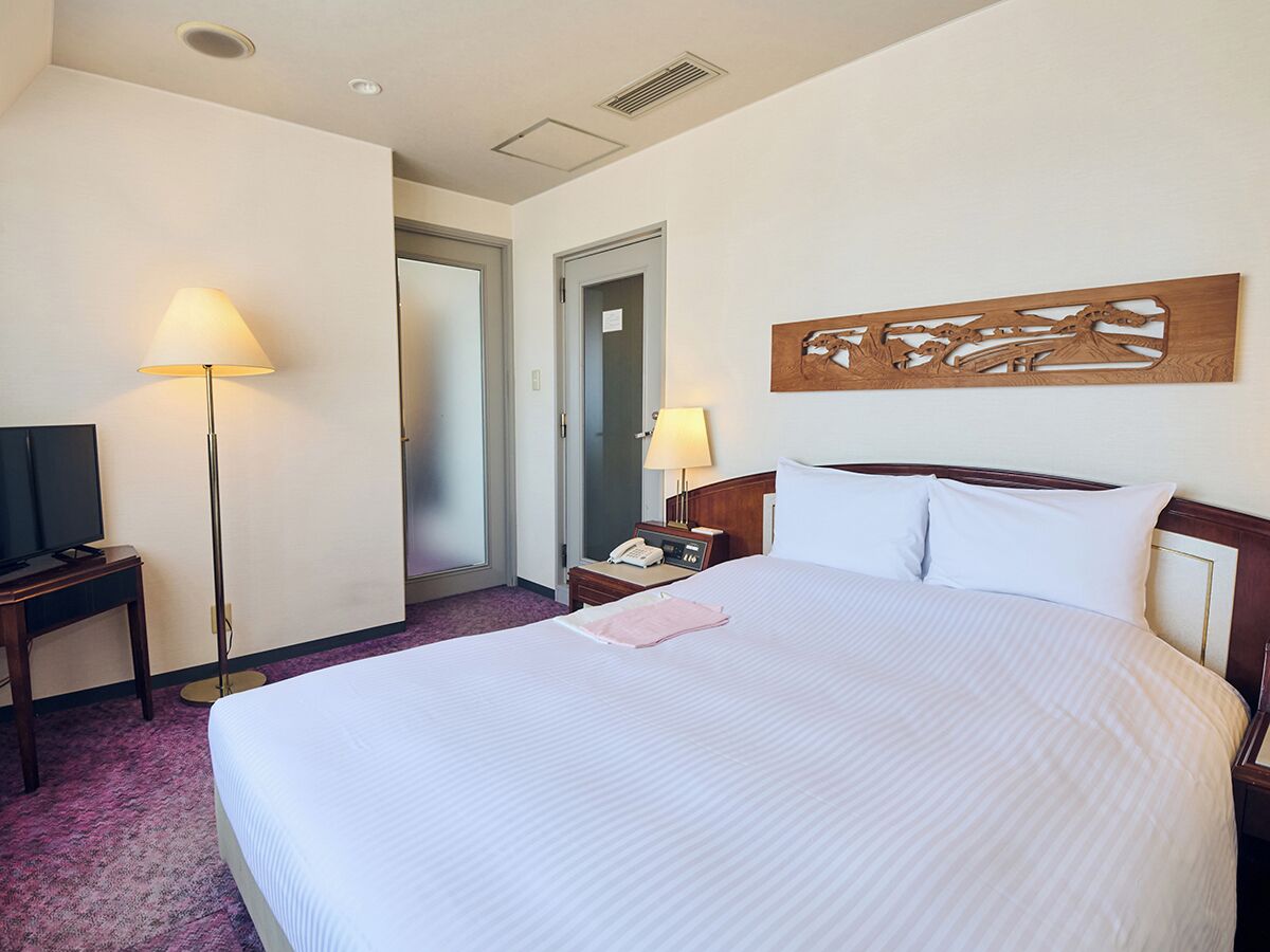 Habitación de hotel con una cama grande, una mesita de noche con lámpara, un televisor de pantalla plana y una obra de arte de madera sobre la cama.