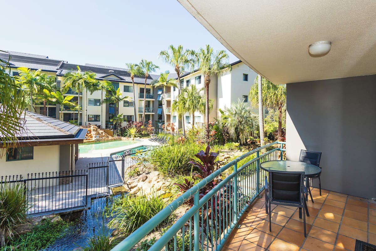 Un balcon avec une piscine, des palmiers et une vue sur un immeuble à plusieurs étages.