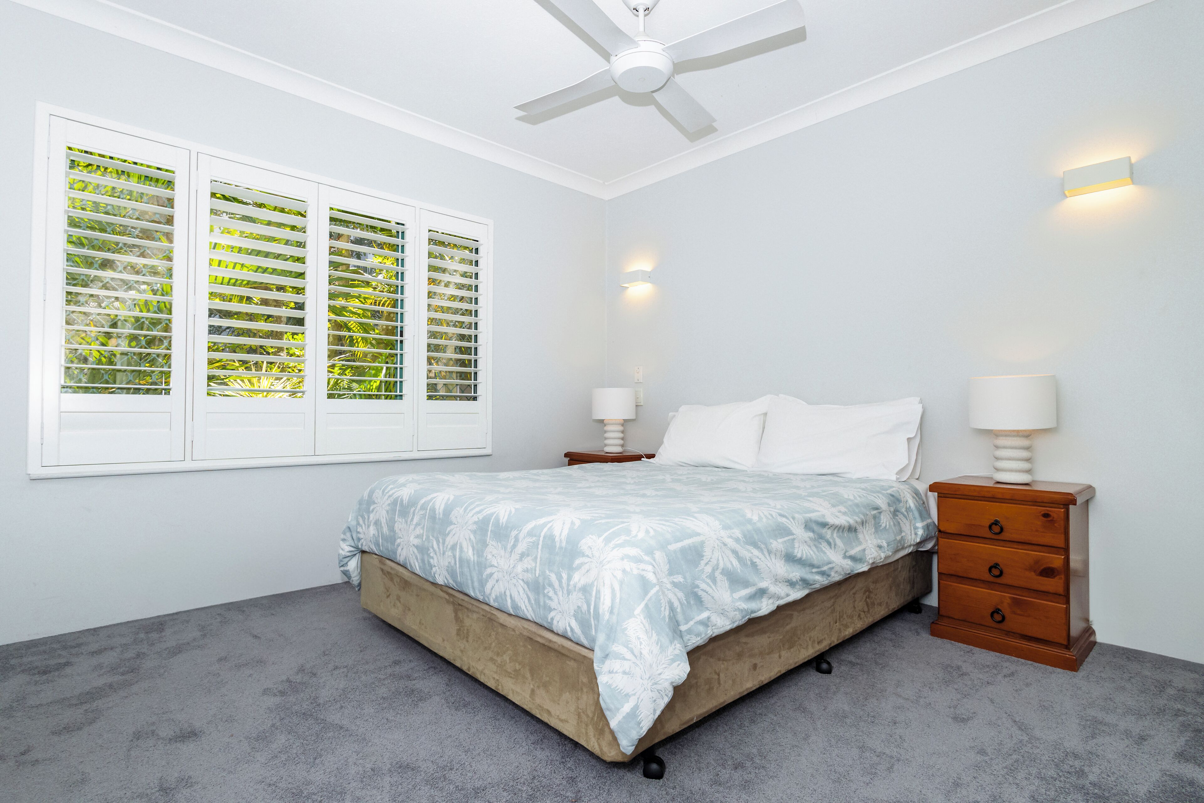 A bedroom with a bed, a nightstand, a ceiling fan, and a window with blinds.