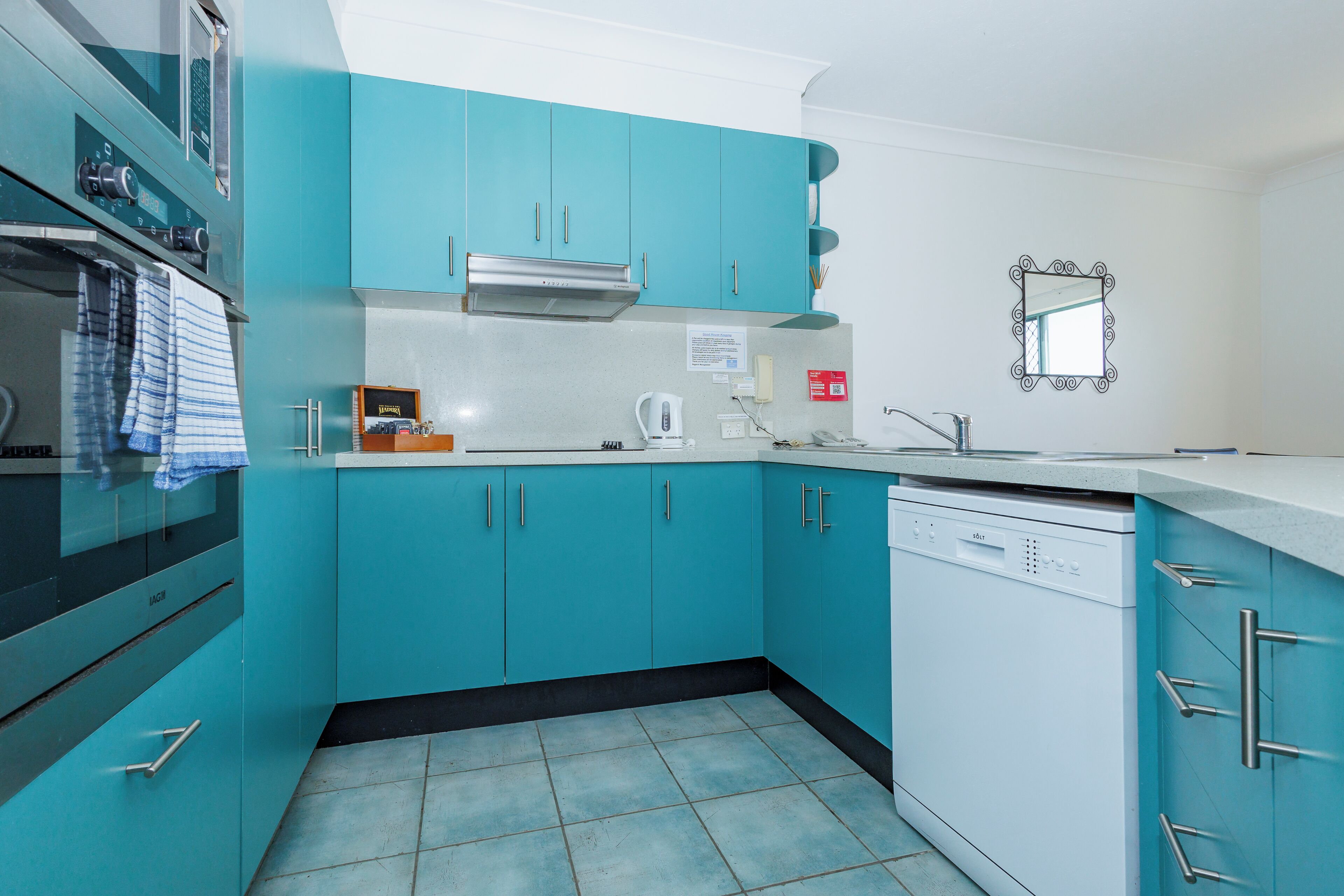 Una cocina con armarios color turquesa, lavavajillas y estufa.