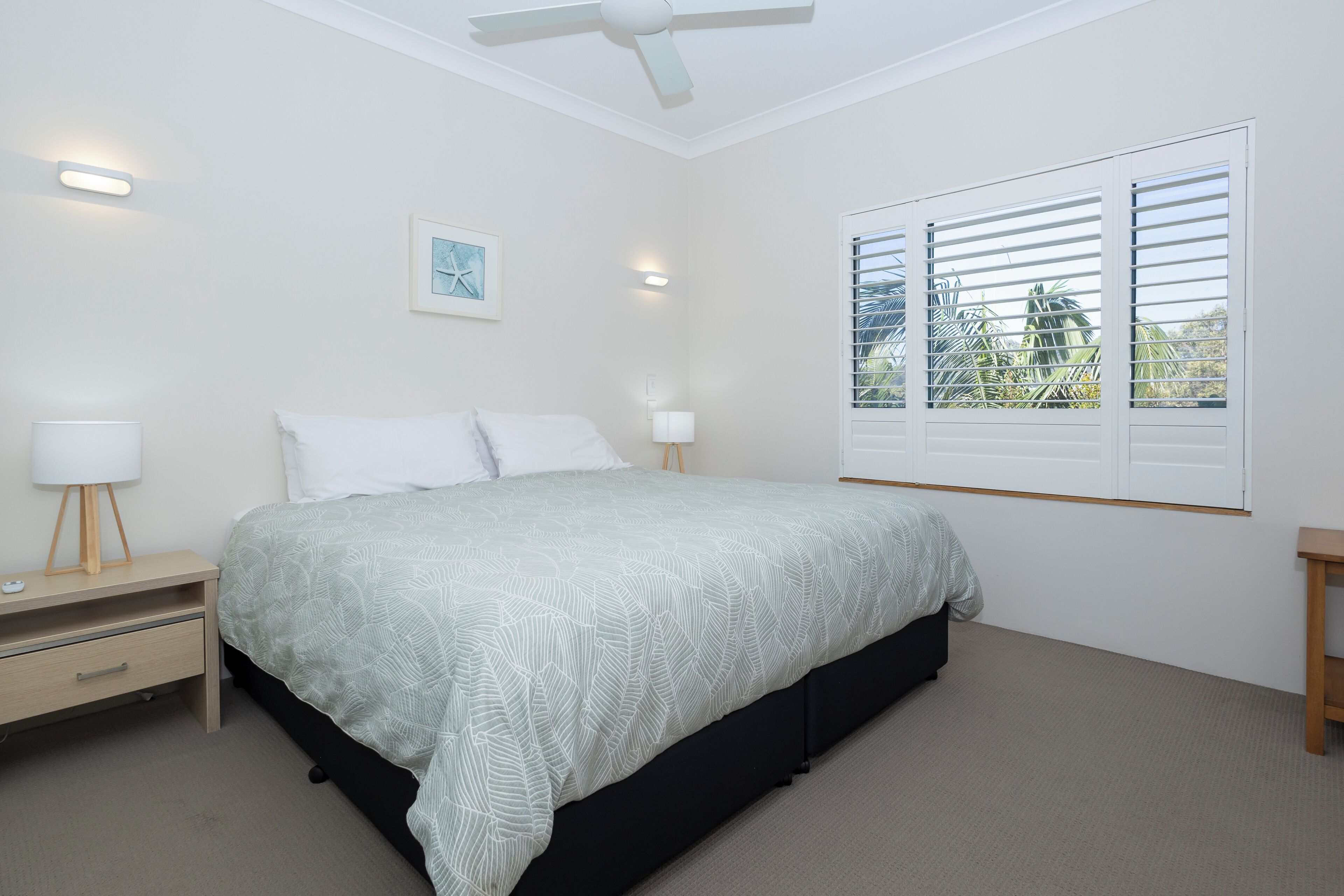 A bedroom with a bed, bedside tables, a ceiling fan, and a window with blinds.