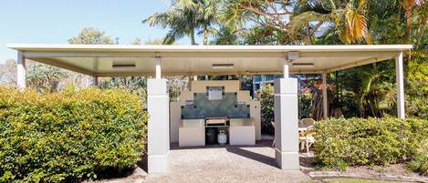 A covered outdoor area with a seating arrangement, surrounded by lush greenery and palm trees.