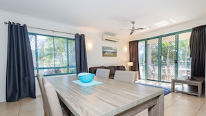 A dining area with a wooden table, chairs, and a blue bowl. There is a sofa and a TV table in the background. - Currumbin Sands Holiday Apartments (Palm Beach)