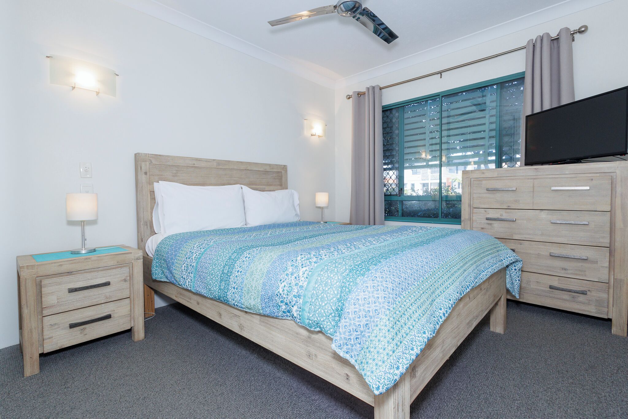 Een slaapkamer met een bed, nachtkastjes, een televisie en een raam met gordijnen.