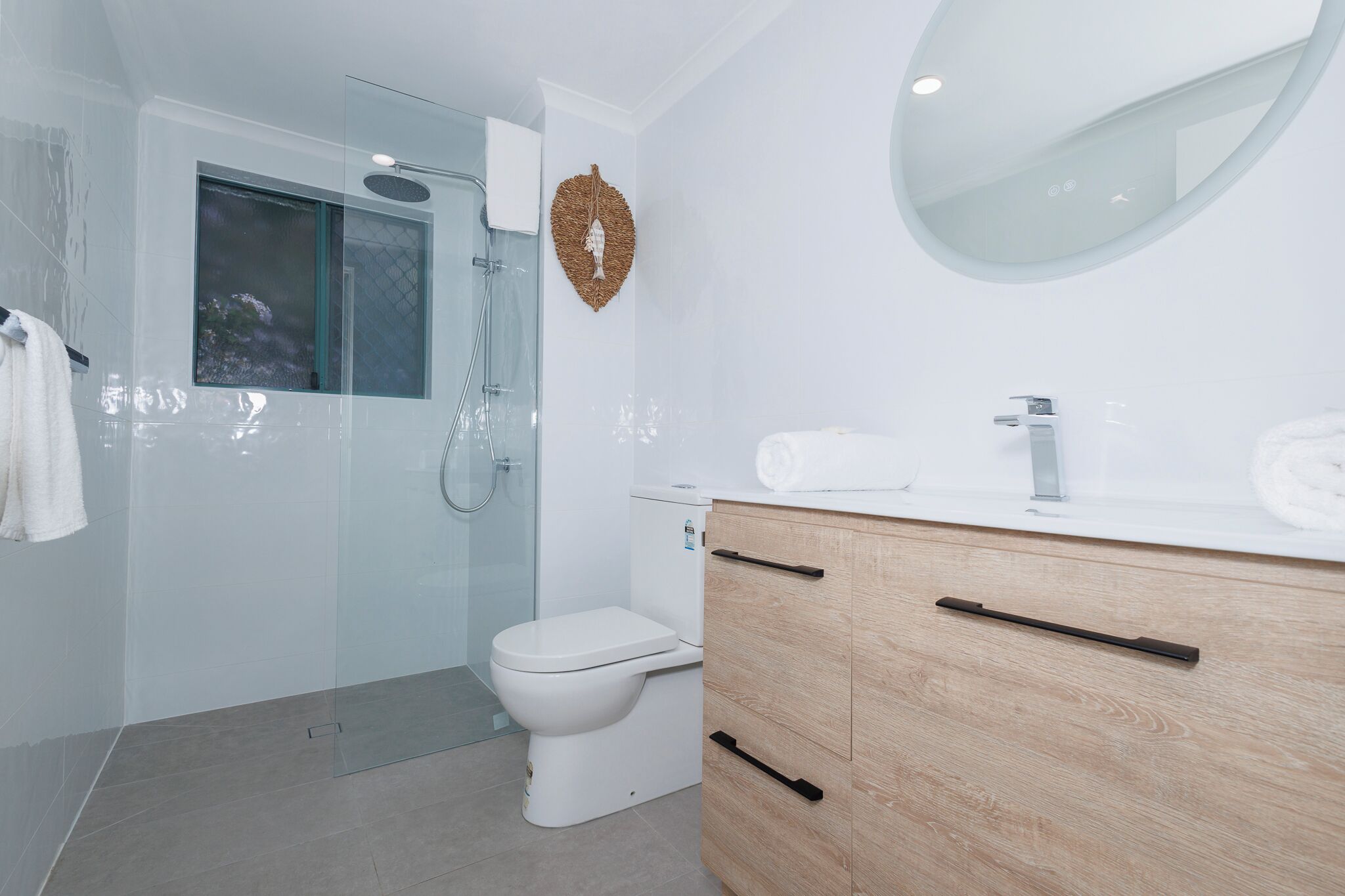 A modern bathroom with a glass-enclosed shower, a white toilet, and a wooden vanity with a mirror.