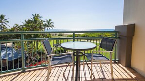 A balcony with a table and two chairs, overlooking a green landscape and a clear sky. - Currumbin Sands Holiday Apartments (Palm Beach)