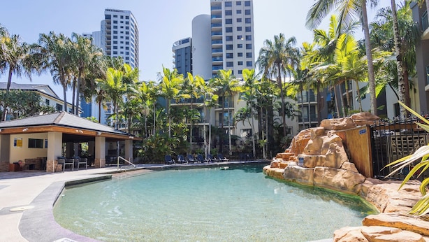A clear swimming pool with lounge chairs, palm trees, and a rocky feature. - Currumbin Sands Holiday Apartments (Palm Beach)