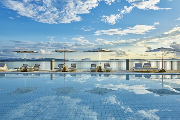 A swimming pool with lounge chairs and umbrellas, surrounded by a fence and mountains in the background. - COMO Point Yamu, Phuket (Pa Klok)