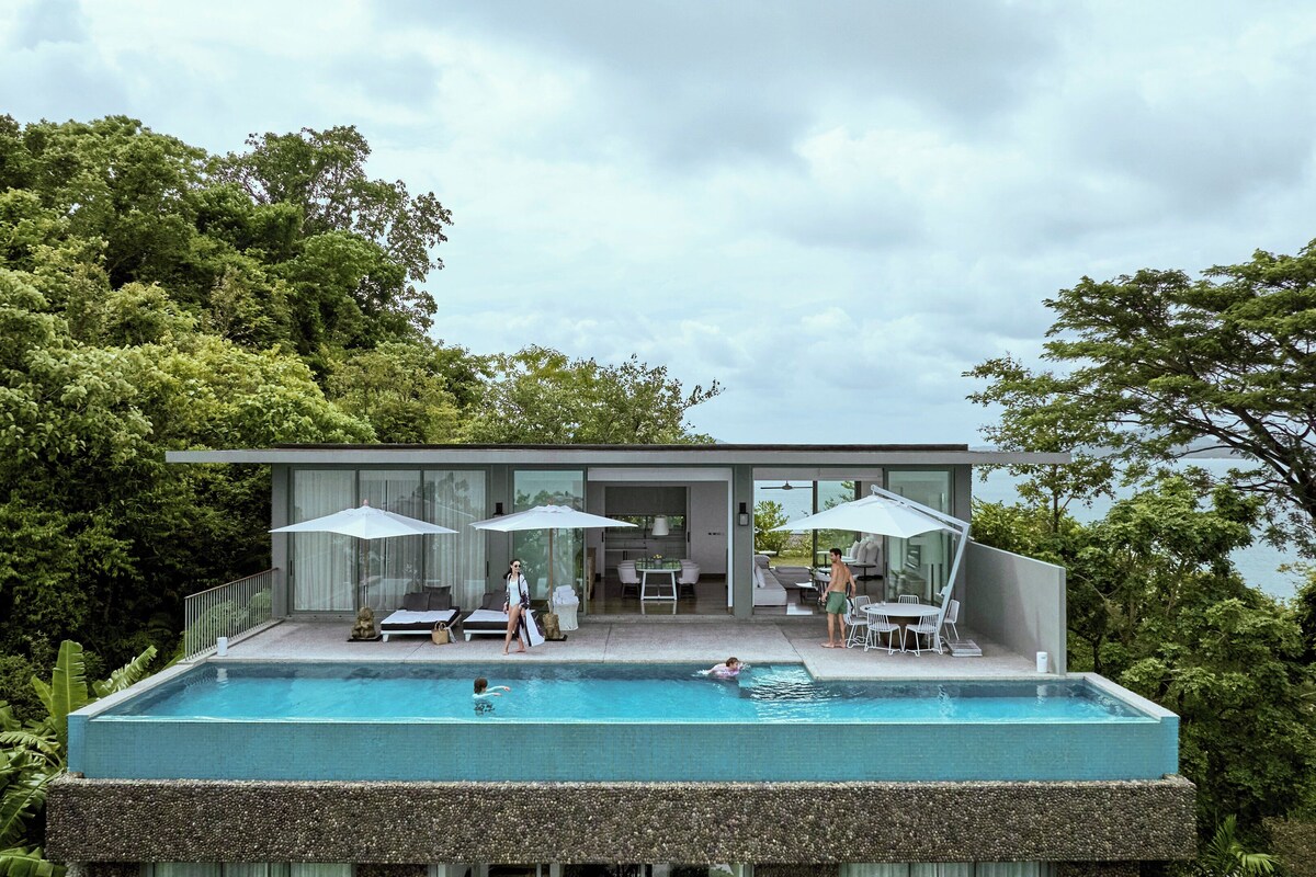 A modern house with a swimming pool, outdoor seating, and a view of the surrounding greenery.