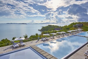 A pool area with lounge chairs and umbrellas, overlooking a body of water and greenery.