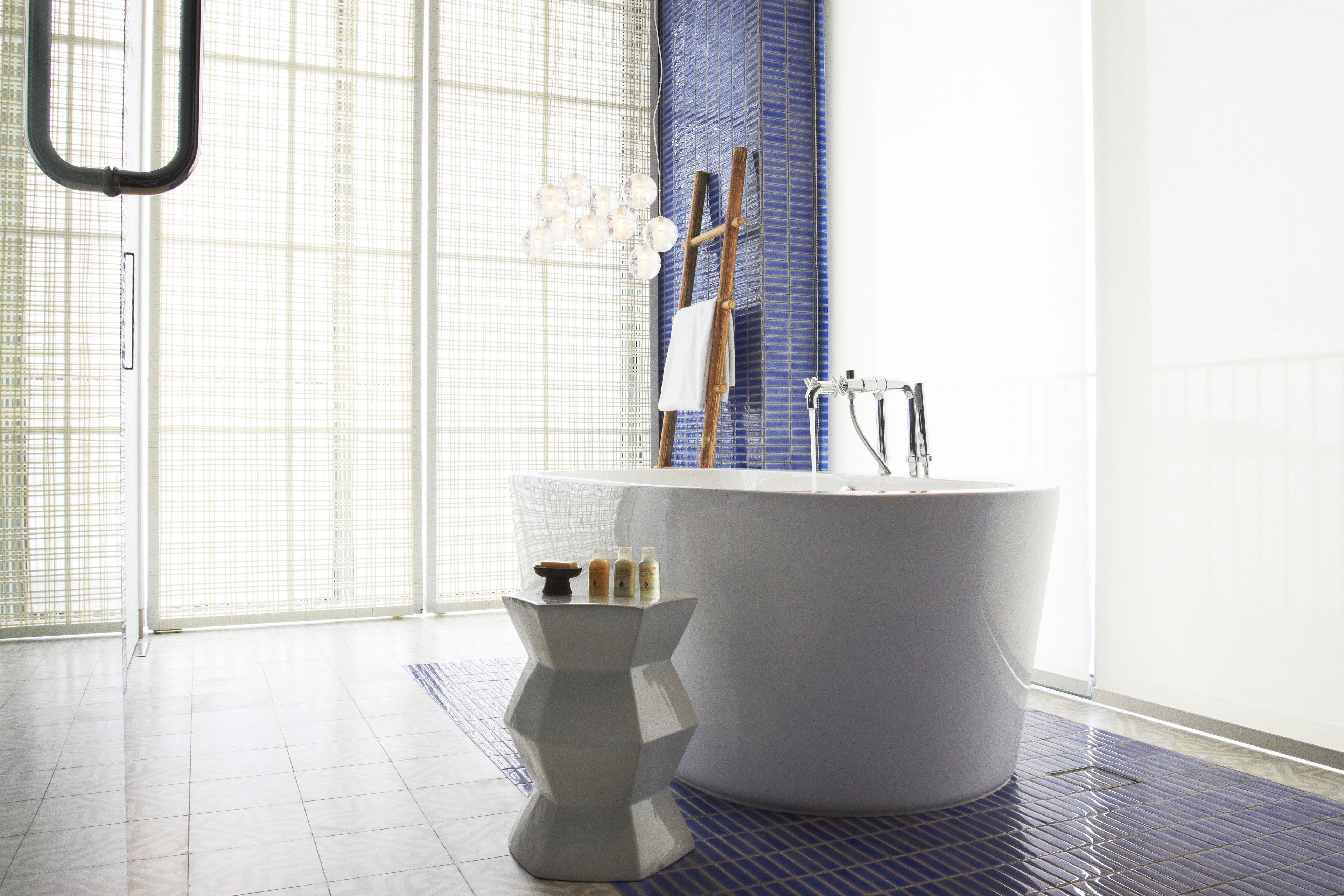 A modern bathroom with a freestanding bathtub, a small white pedestal, and a wooden ladder leaning against the wall.