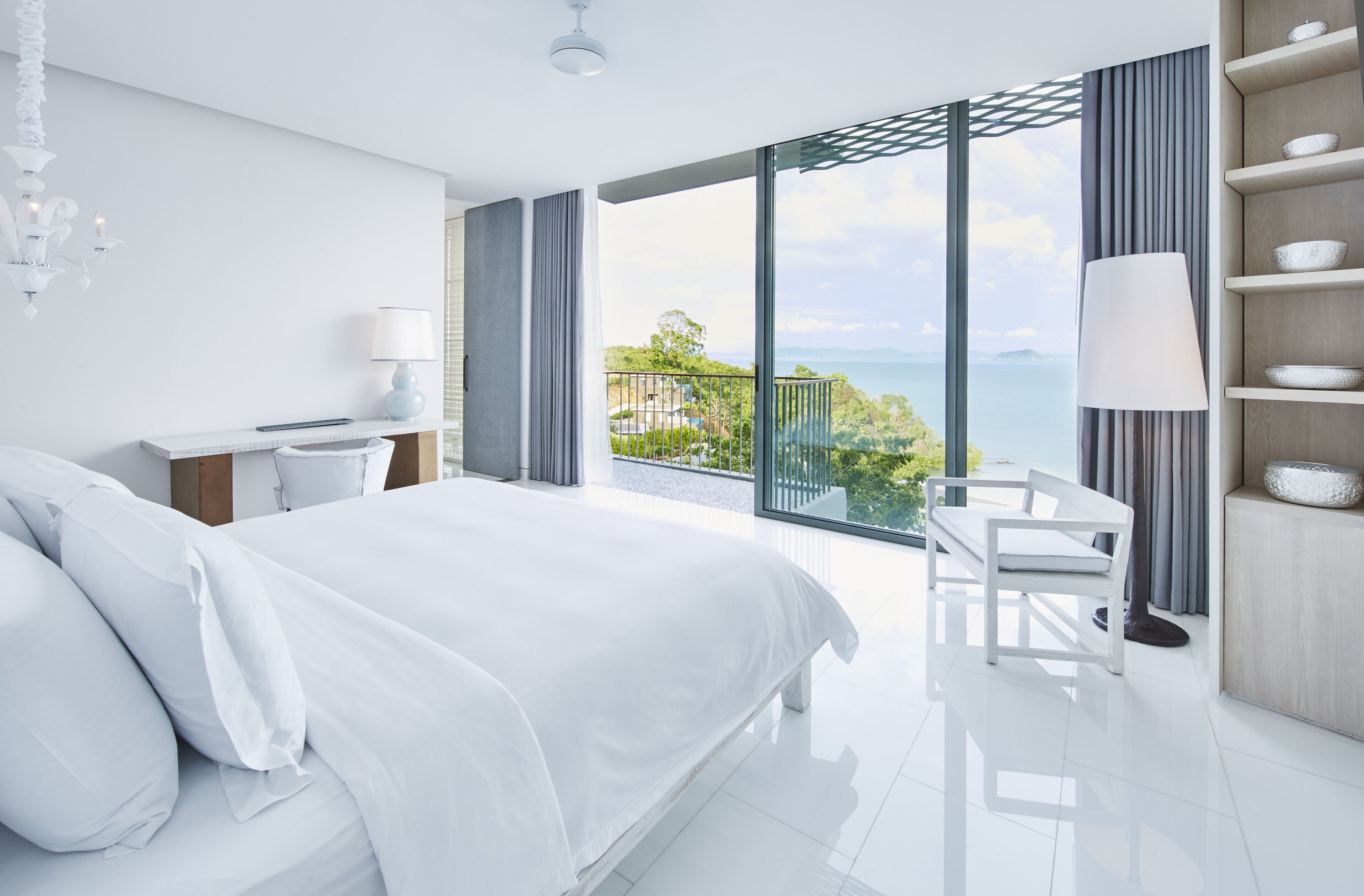 A modern hotel room with a large bed, a desk, and a view of the ocean.