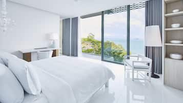 A modern hotel room with a large bed, a desk, and a view of the ocean.