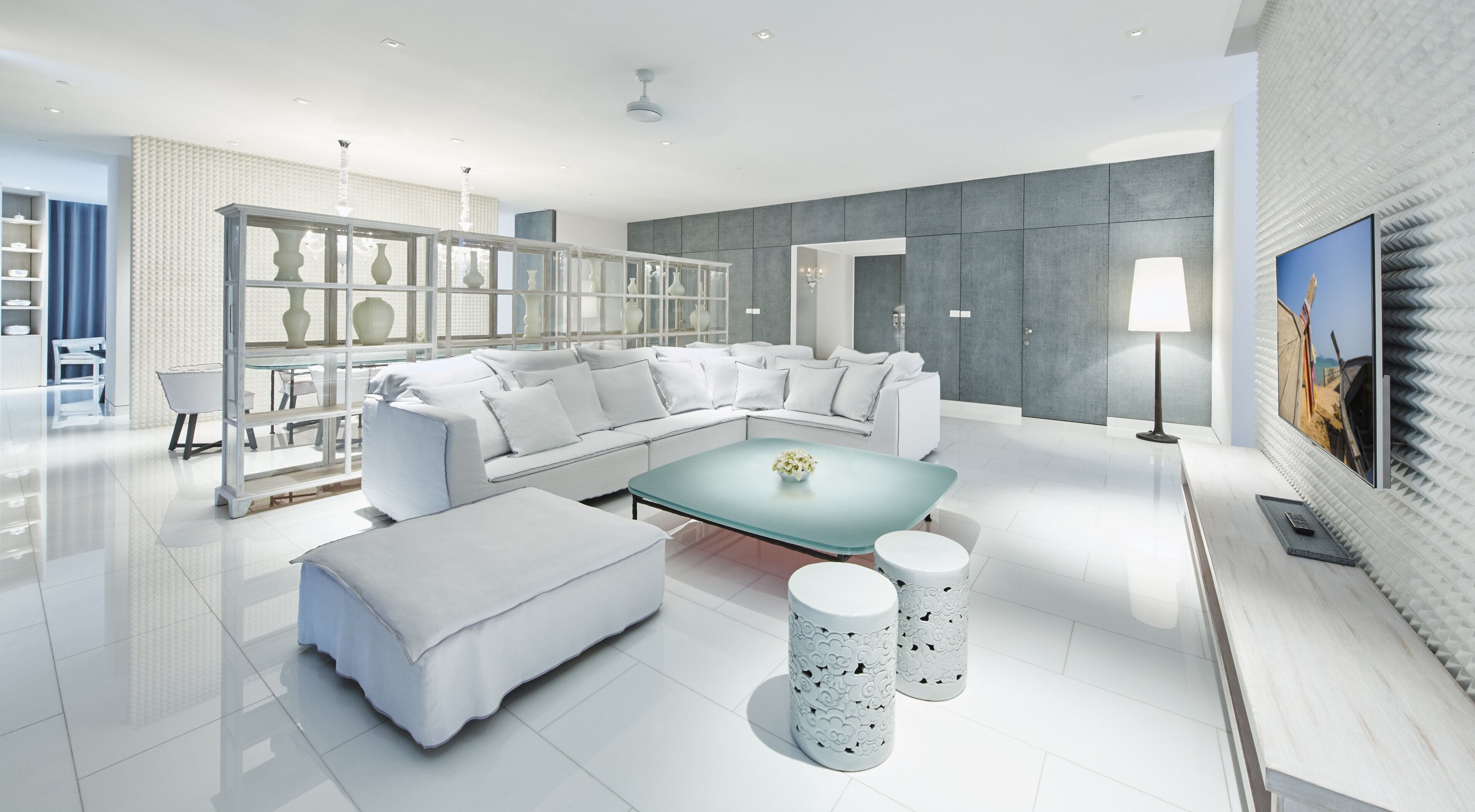 Een moderne woonkamer met een modulaire bank, een glazen salontafel en witte decoratieve objecten.