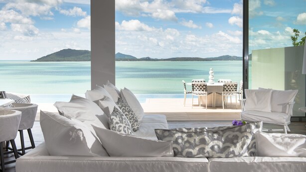 A modern living room with a large window overlooking a turquoise sea and a distant island.