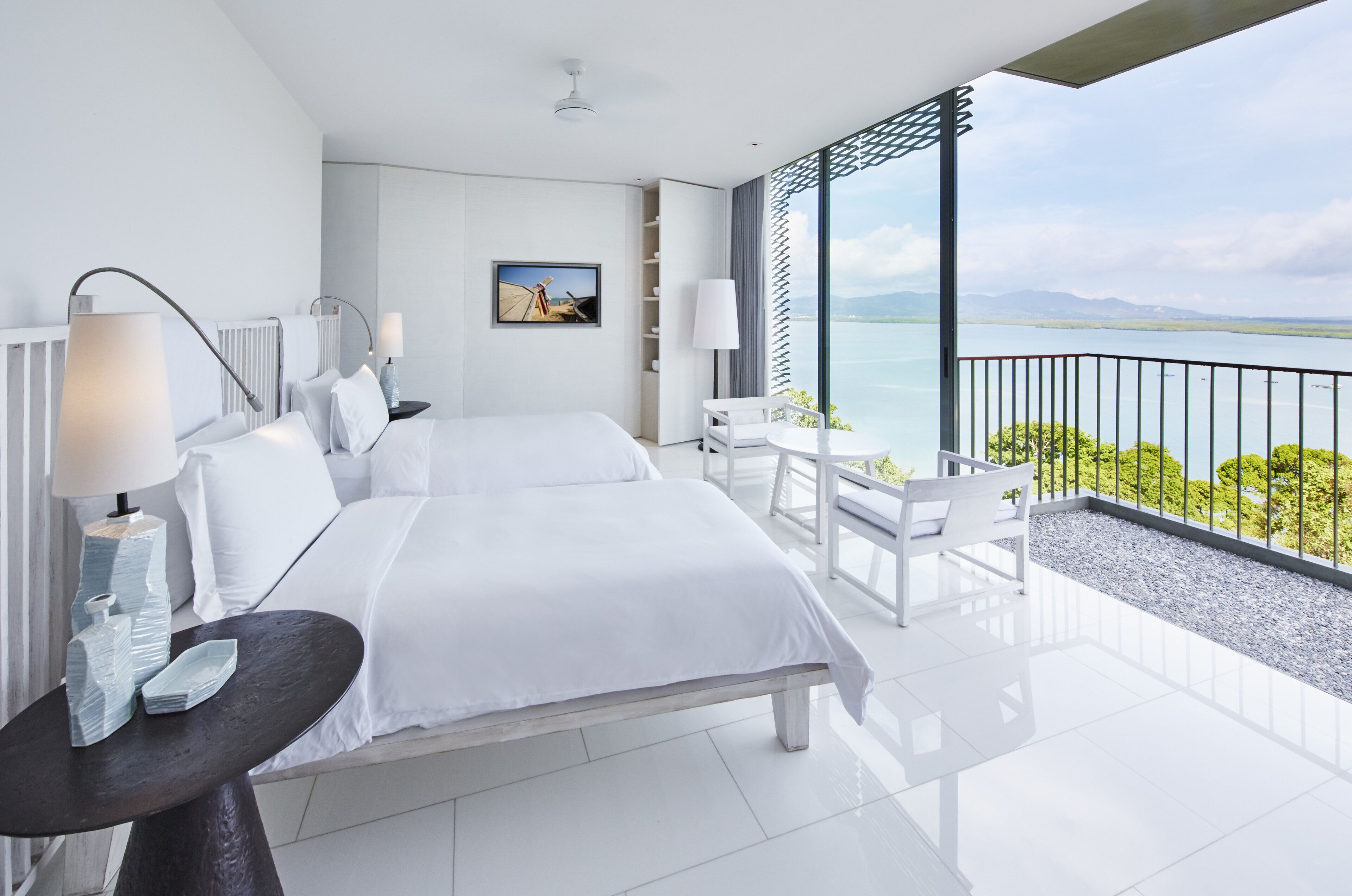 A modern hotel room with a large bed, bedside tables, a desk, and a balcony with a view of the sea.