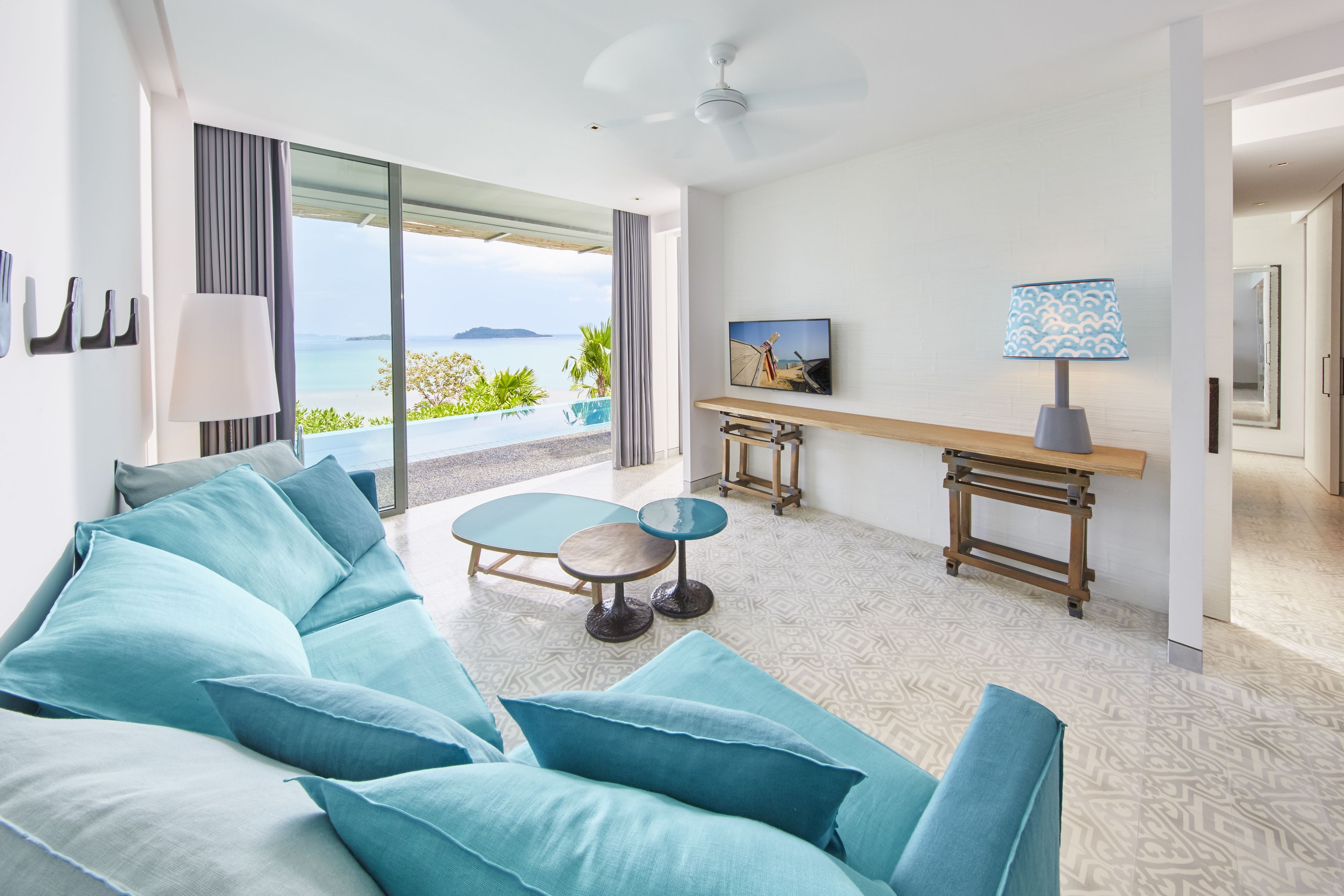 Habitación de hotel moderna con un sofá grande, una mesita, un televisor y vistas al mar.
