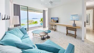 Habitación de hotel moderna con un sofá grande, una mesita, un televisor y vistas al mar.