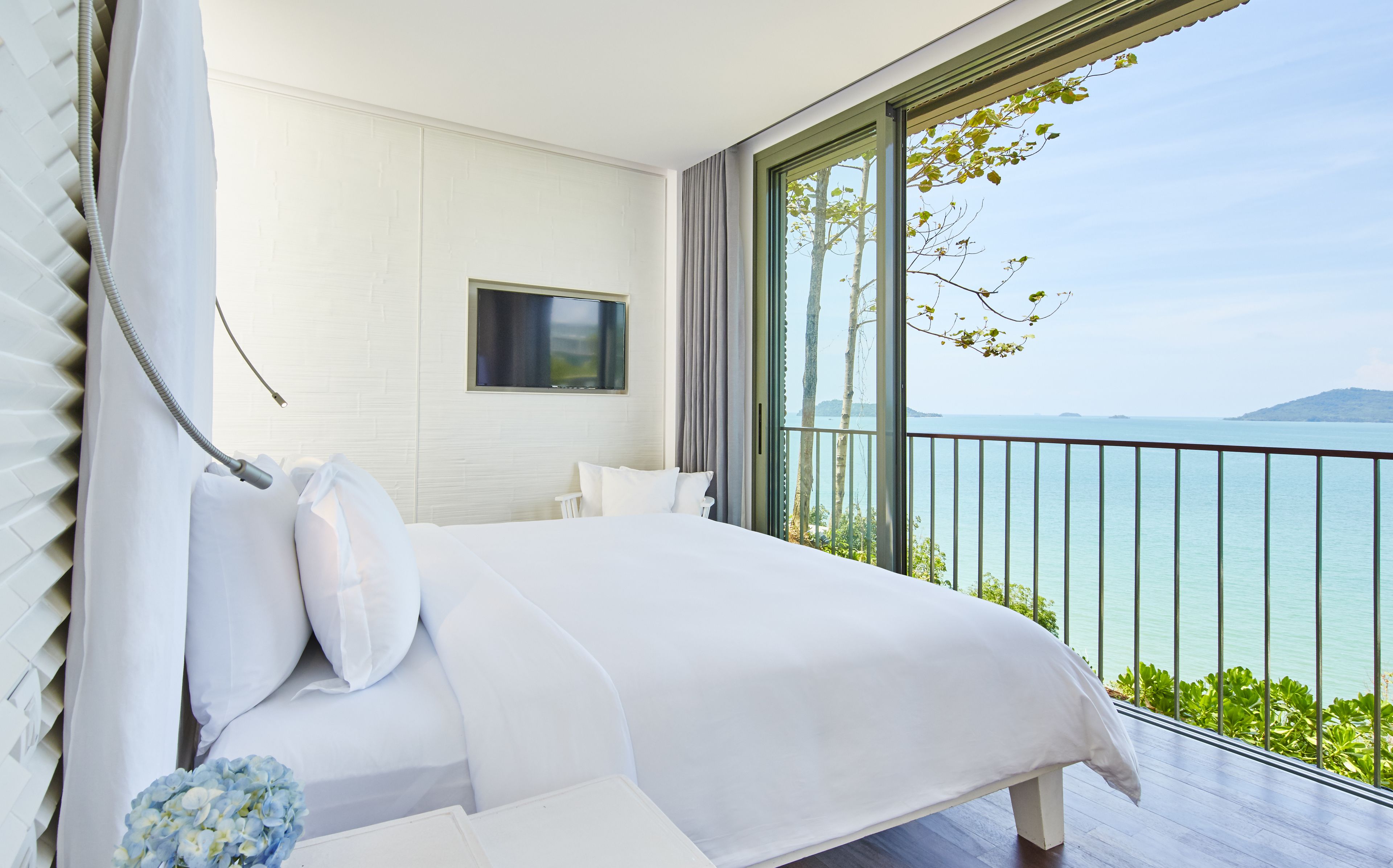 Een slaapkamer met een groot bed, een aan de muur bevestigde televisie en een balkon met uitzicht op zee.