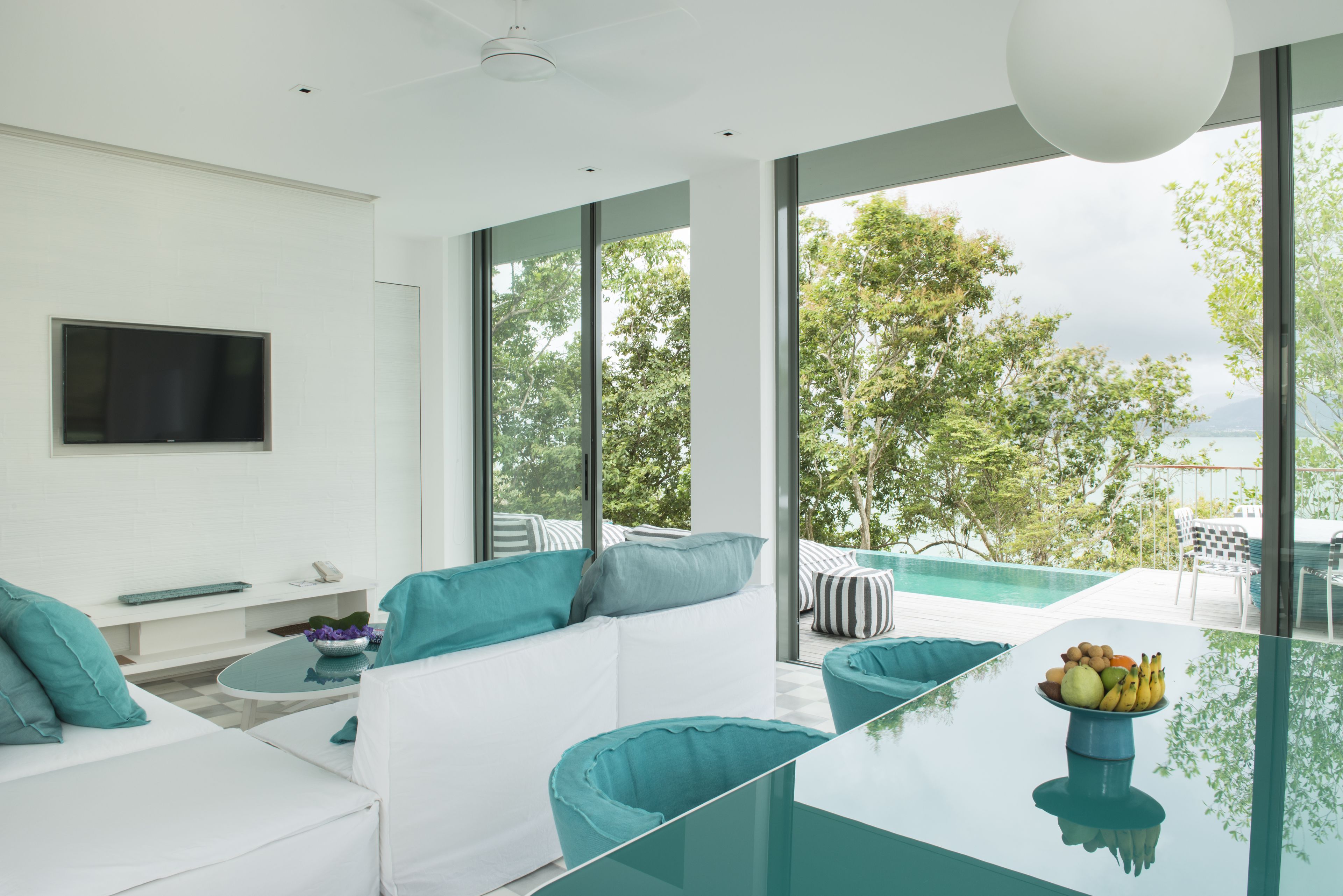 A modern living room with a glass coffee table, white sofas, and teal cushions.