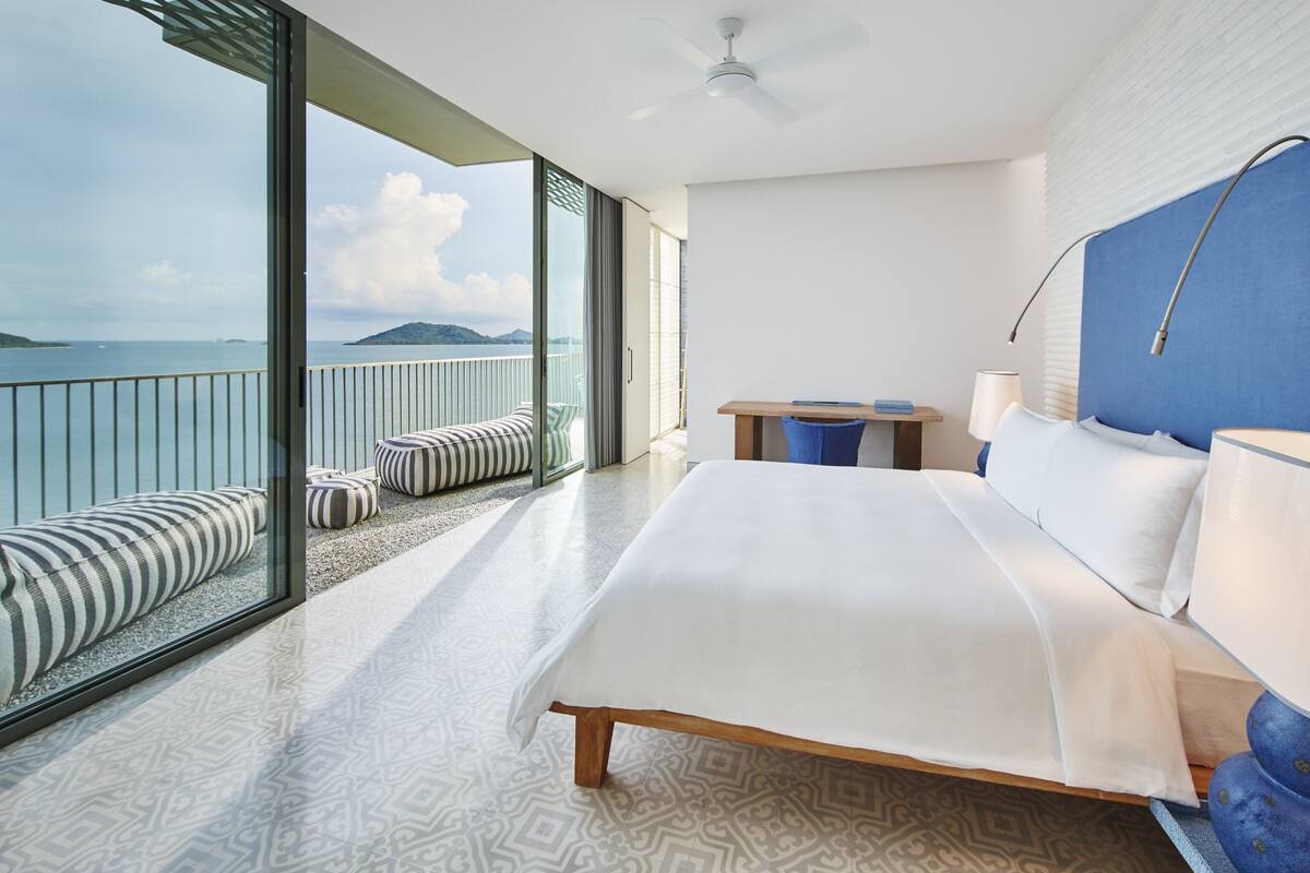 Een moderne hotelkamer met een groot bed, een balkon met zitplaatsen en uitzicht op zee.