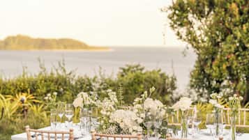 A table set for dining with a view of the sea and greenery.