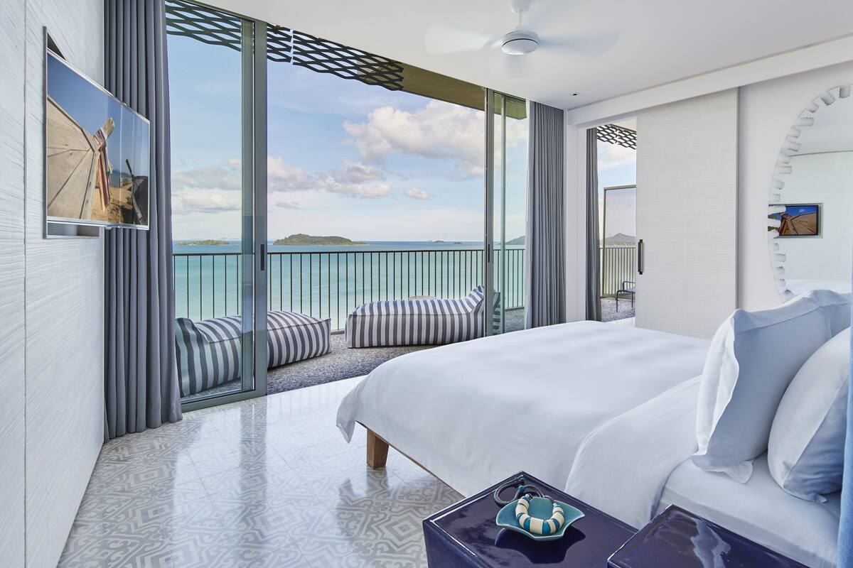Een moderne hotelkamer met een groot bed, uitzicht op de zee en een balkon met een hekwerk.