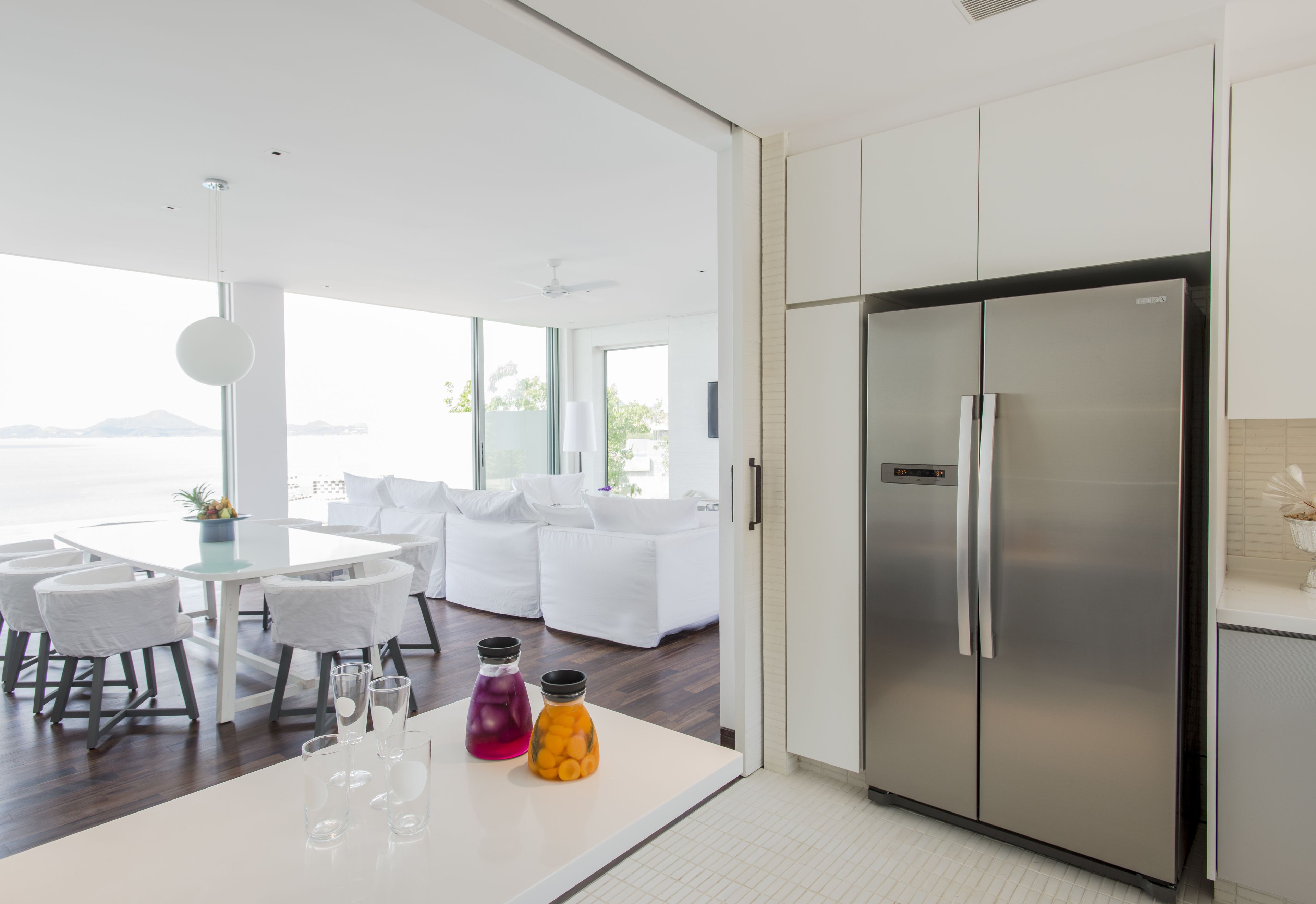 Una cocina moderna con refrigerador de acero inoxidable, armarios blancos y un comedor con mesa y sillas blancas.