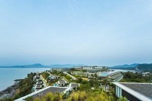 A coastal hotel with modern architecture, a swimming pool, and a view of the sea and mountains.