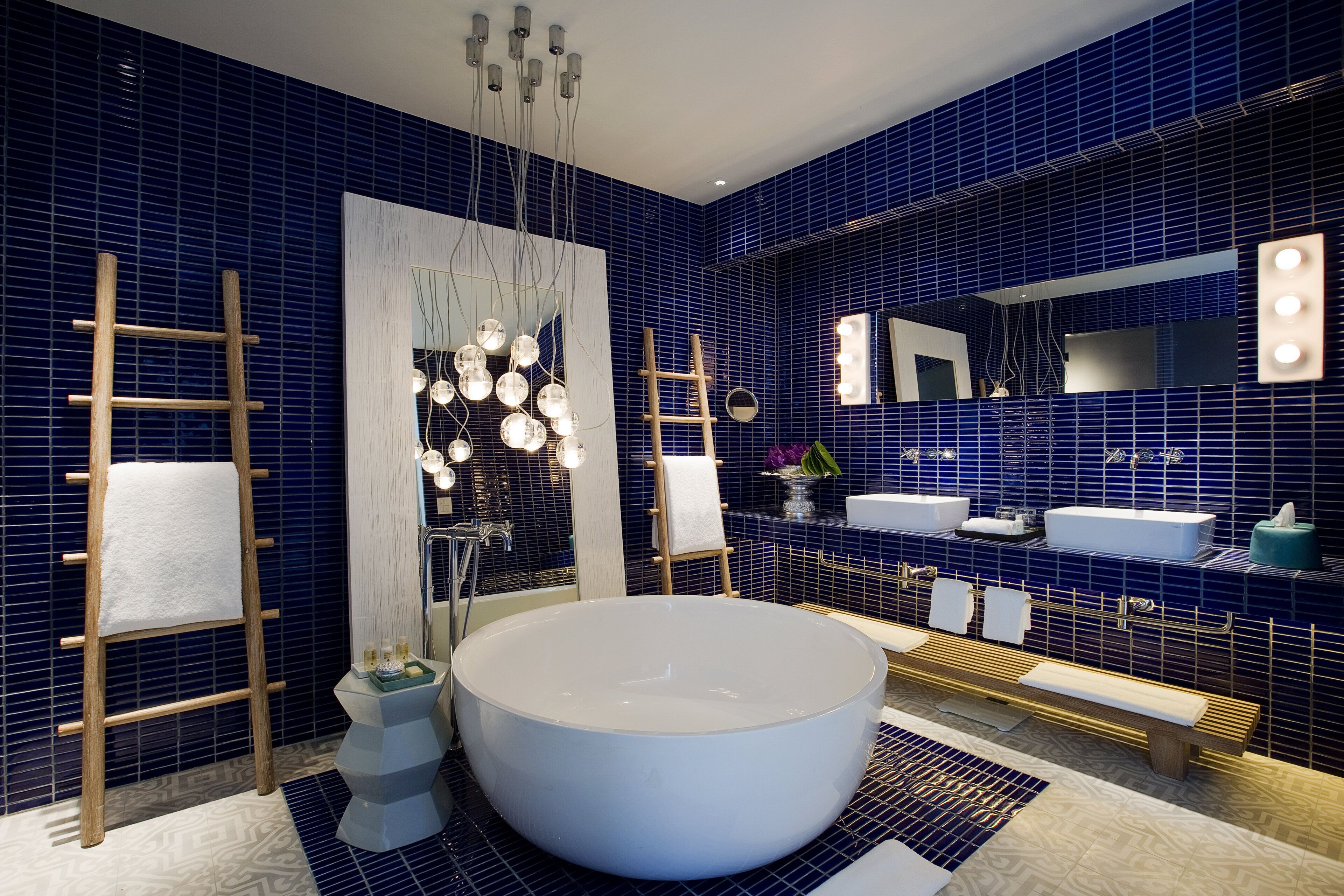 A modern bathroom with a large bathtub, two sinks, a vanity with a mirror, and a wooden ladder.