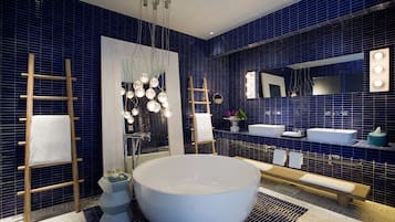 A modern bathroom with a large bathtub, two sinks, a vanity with a mirror, and a wooden ladder.