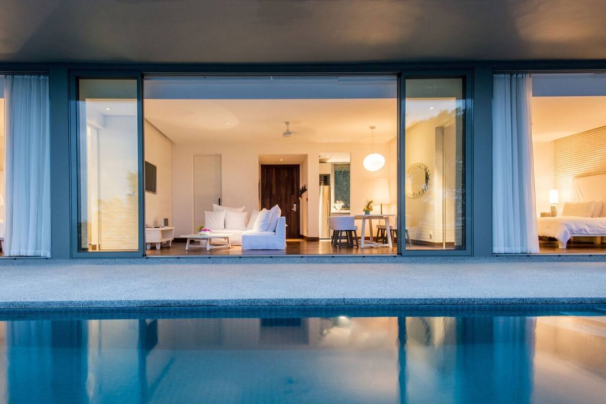 Een modern hotel met een zwembad, een woonkamer met een bank en een salontafel, en een eetgedeelte met een tafel en stoelen.