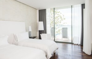 A hotel room with two beds, a large window with a view, a lamp, and a small table.