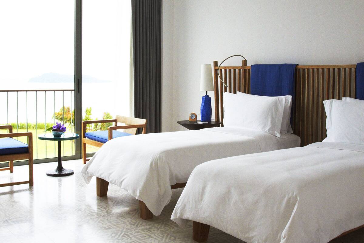 Een hotelkamer met twee bedden, een balkon met een tafel en stoelen, en uitzicht op de omgeving.