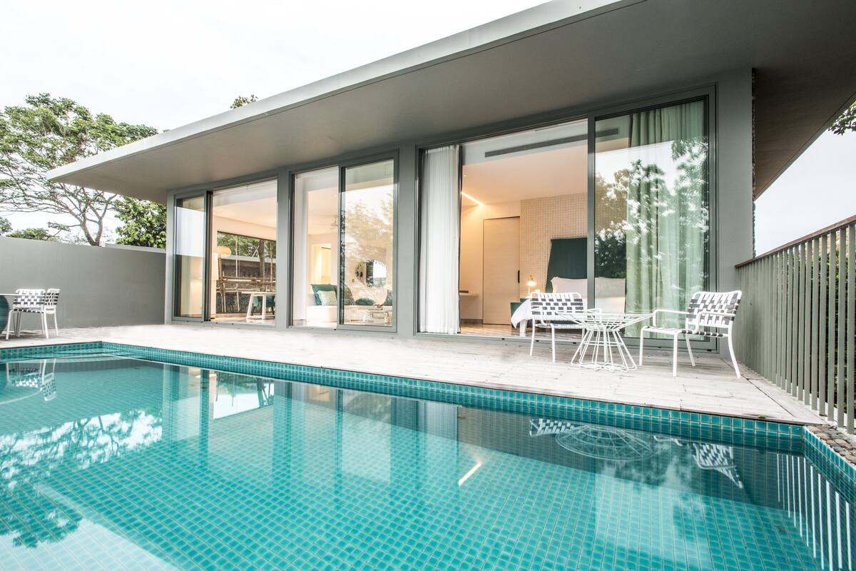 Een modern buitenzwembad met een helderblauw zwembad, witte ligbedden en een glazen patio.