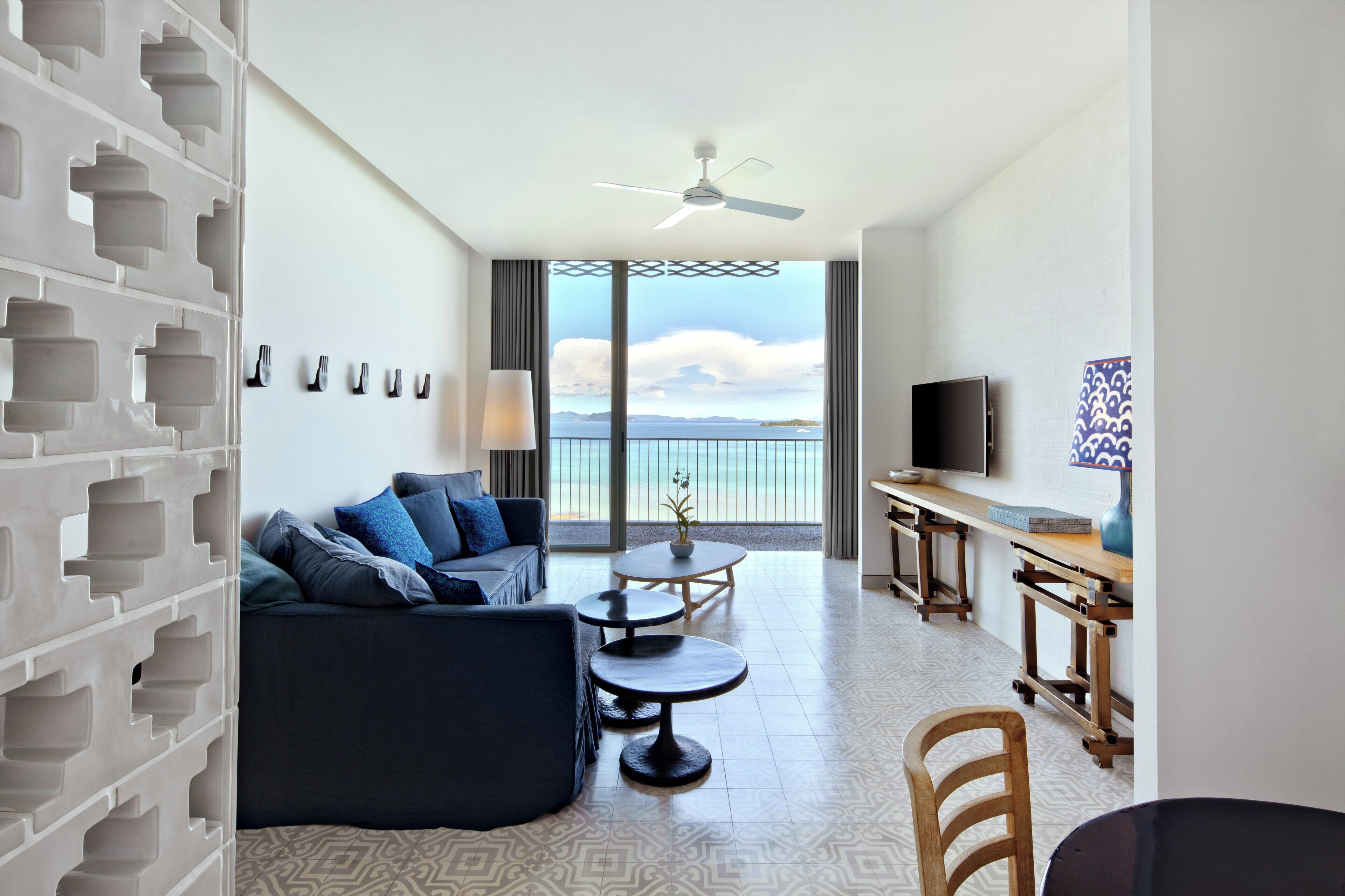 Una habitación de hotel moderna con balcón, un sofá, una mesa de comedor y un televisor.