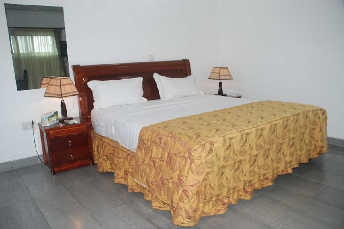 A neatly made bed with a wooden headboard, two bedside lamps, a nightstand, and a mirror on the wall.