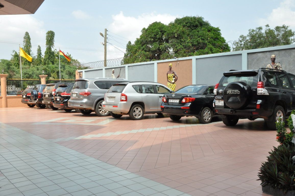 A parking lot with several cars, a statue, and flags.