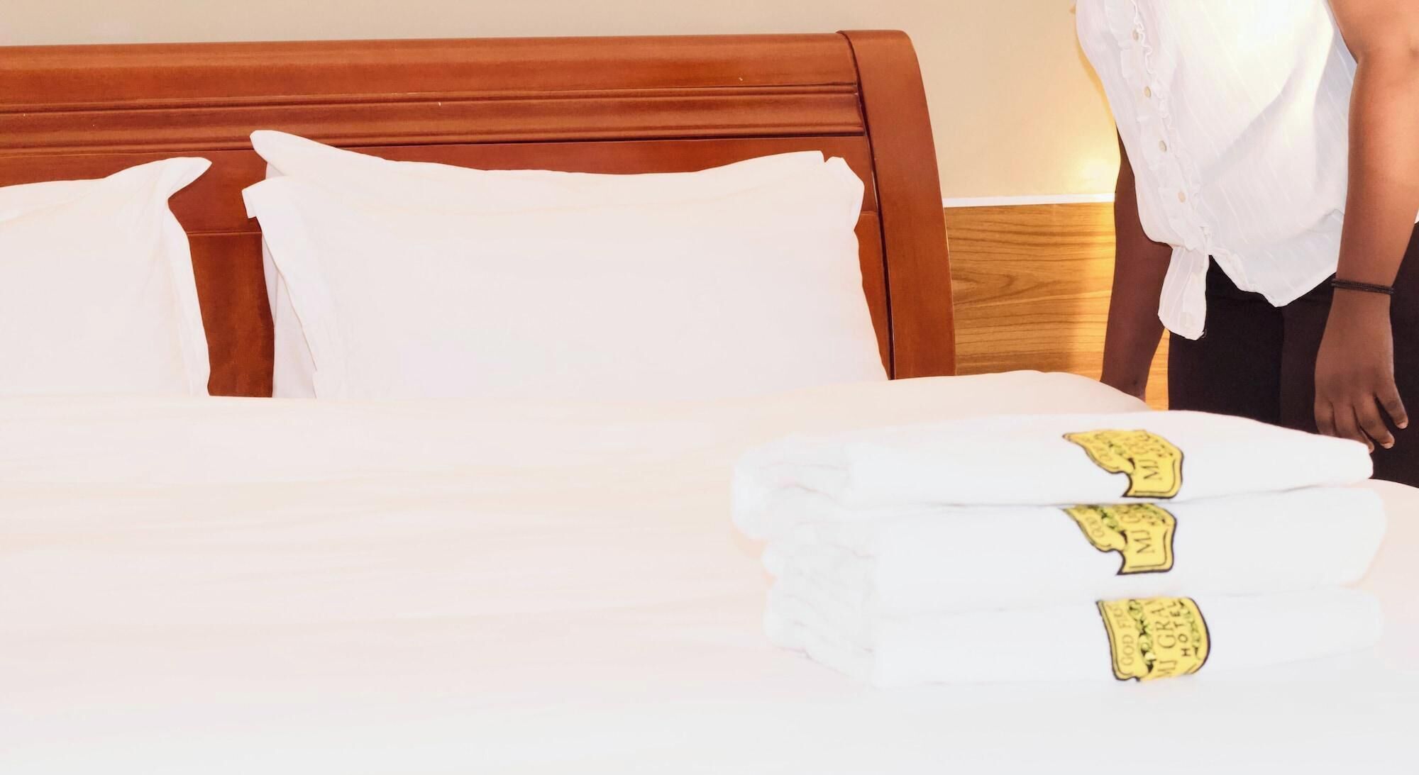 A neatly made bed with white linens and a folded towel with a hotel logo.