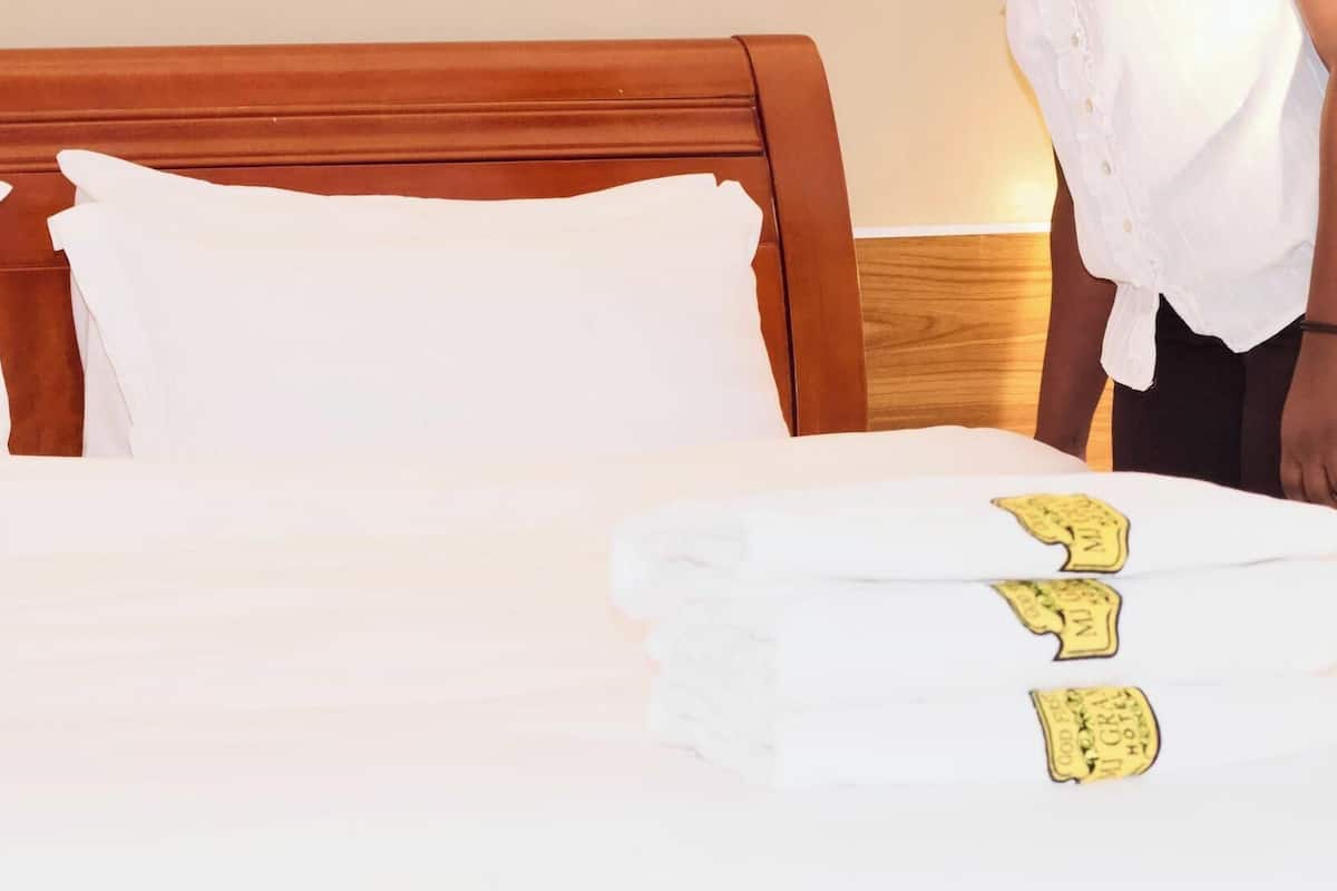 A neatly made bed with white linens and a folded towel with a hotel logo.