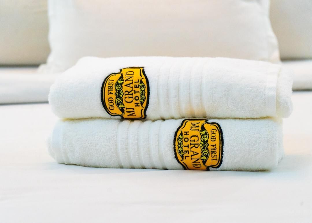 Dos toallas blancas dobladas con etiquetas bordadas que dicen 'God First MI GRAND HOTEL'.