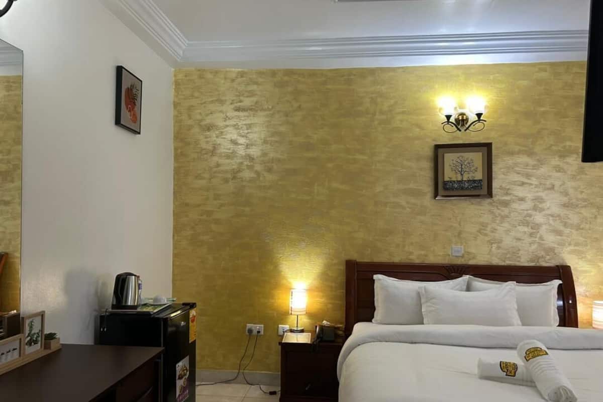 A hotel room with a bed, a desk, a nightstand, a lamp, and a wall-mounted light fixture.