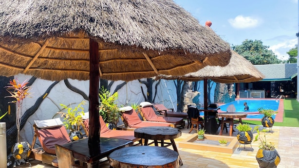 A poolside area with lounge chairs, a table, and a thatched umbrella. - MJ Grand Hotel (Accra)