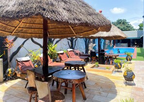 A poolside area with lounge chairs, a table, and a thatched umbrella. - MJ Grand Hotel (Accra)