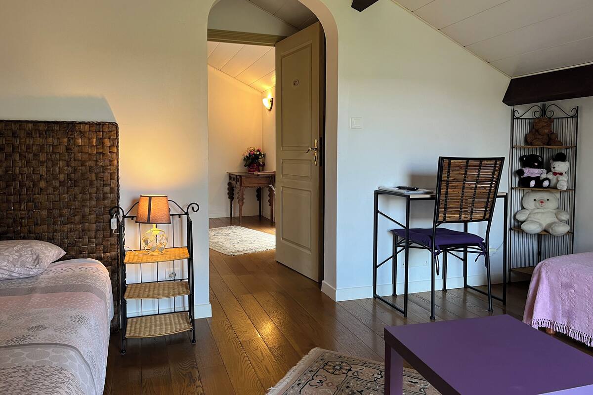 A cozy room with a bed, a desk, and a chair. There is a door leading to another room.