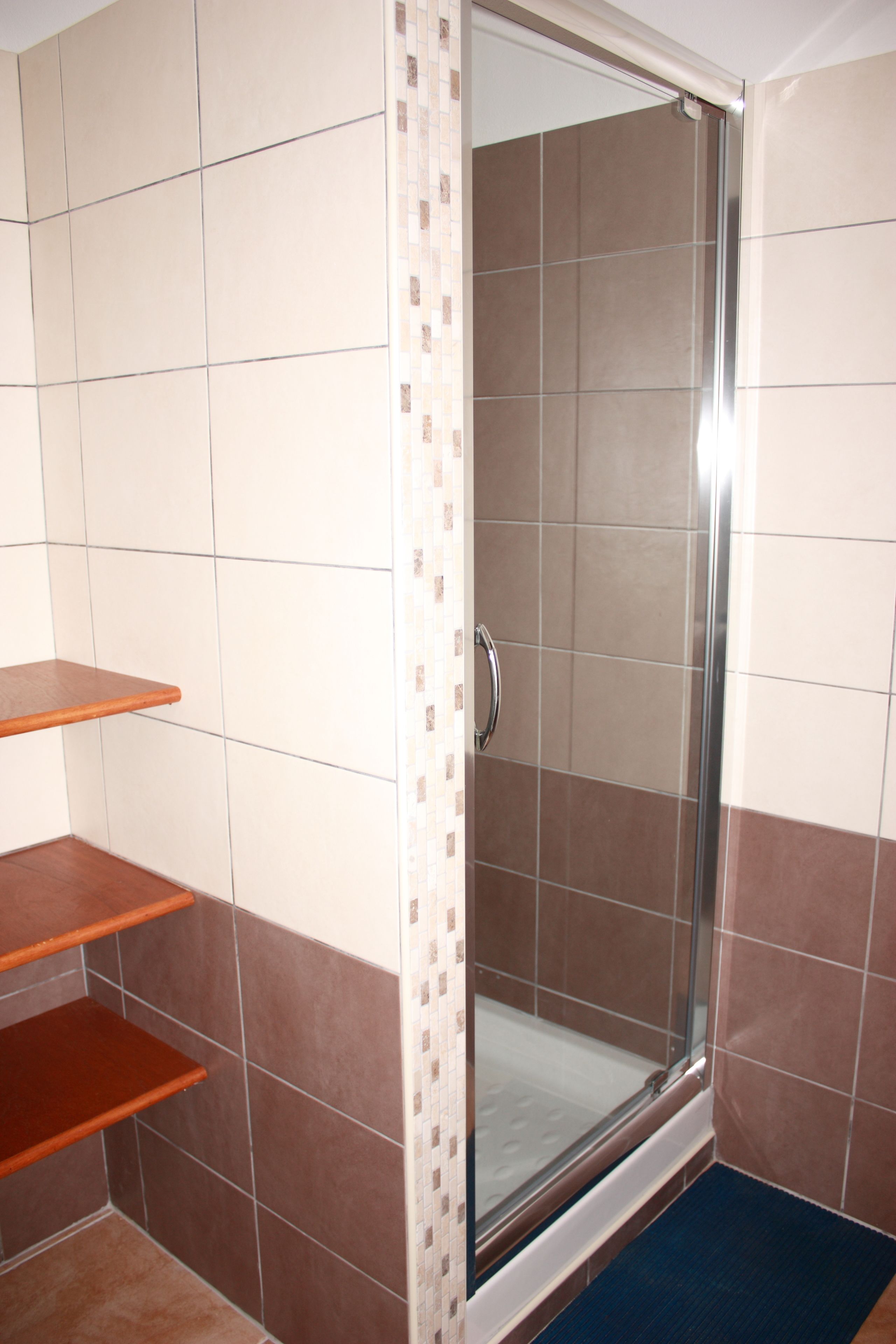 A bathroom with a glass shower enclosure, tiled walls, and wooden shelves.