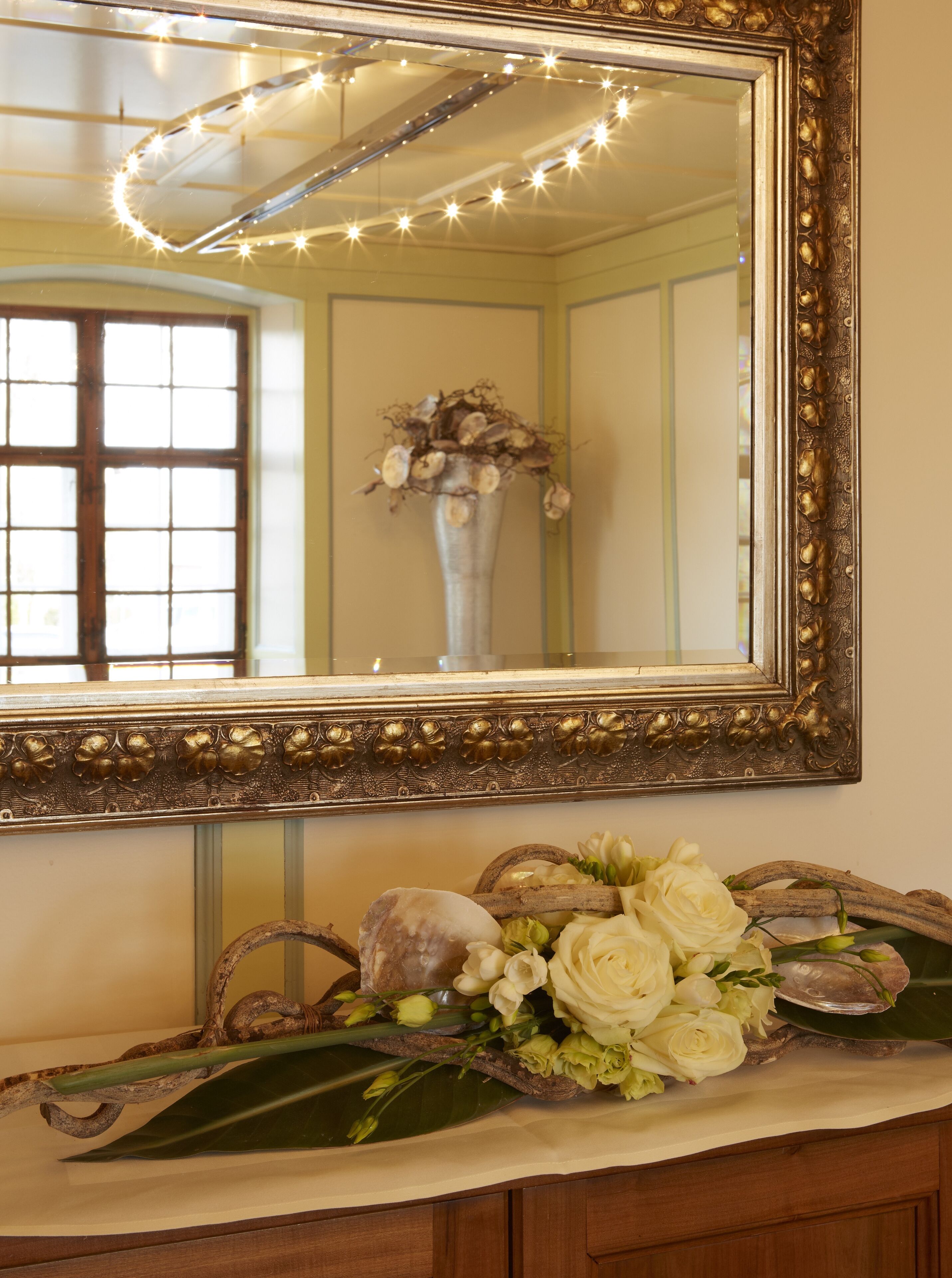 A mirror with a decorative frame, a vase with flowers, and a wooden surface.