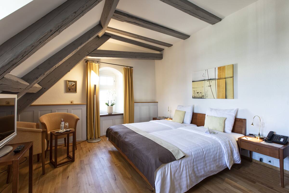 Ein Hotelzimmer mit einem großen Bett, einem Schreibtisch mit Stuhl, einem Fernseher und einem Fenster mit Vorhängen.
