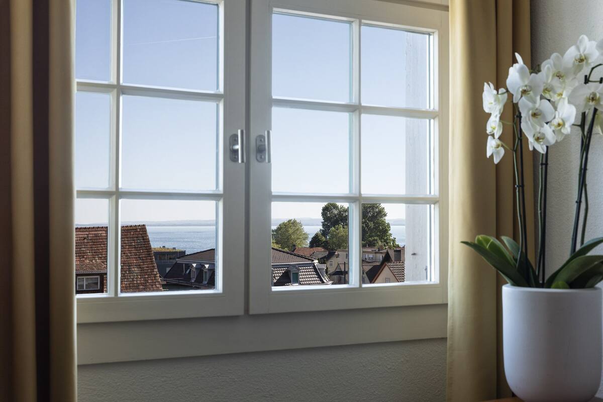 Ein Zimmer mit großem Fenster und Blick auf eine Wohngegend und das Meer.