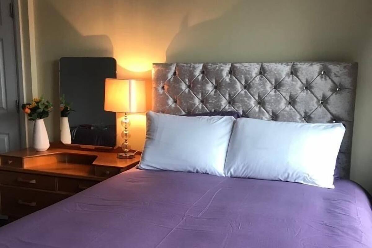 A neatly made bed with a tufted headboard, a bedside table with a lamp, and a mirror.